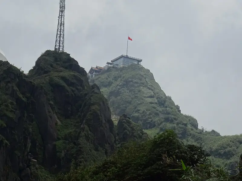 The rocky summit of Fansipan with the flag and the cable car's top buildings on the ridge beside it